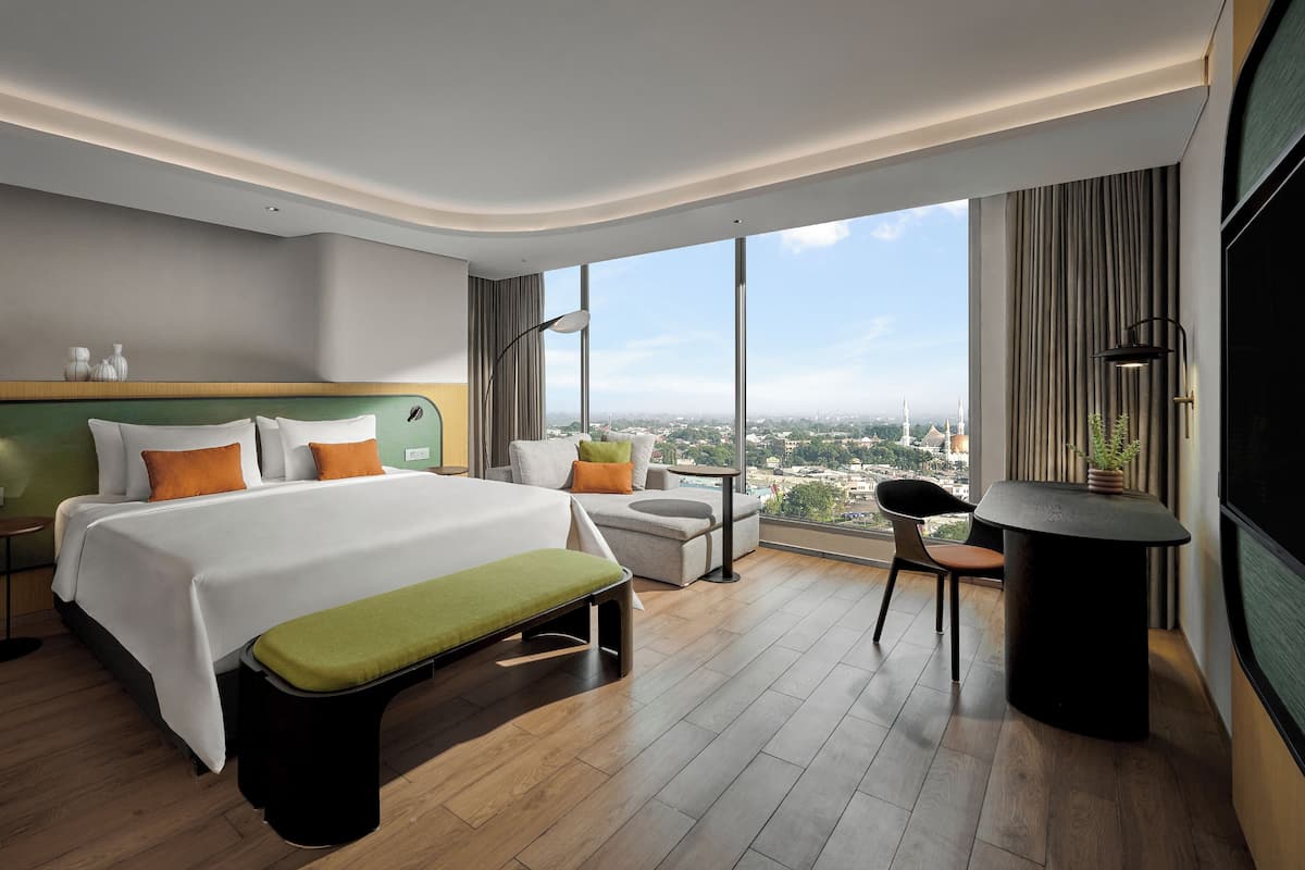 Une chambre d’hôtel moderne avec un grand lit, une banquette, un bureau et une vue sur le paysage urbain.