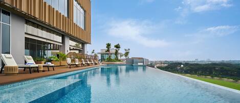 Ein modernes Hotel mit einem Dachpool im Infinity-Stil, Liegestühlen und Blick auf die Stadtlandschaft.