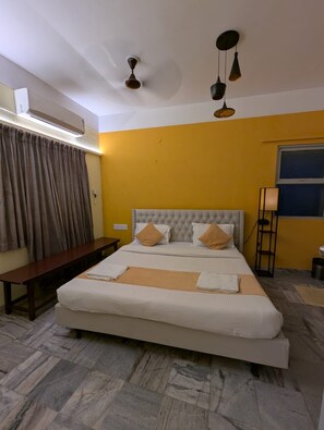 A hotel room with a large bed, a bench, a standing lamp, and a ceiling fan.