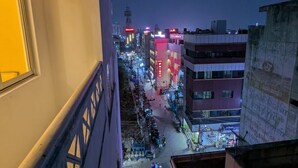 A nighttime cityscape with buildings, streetlights, and a few pedestrians.