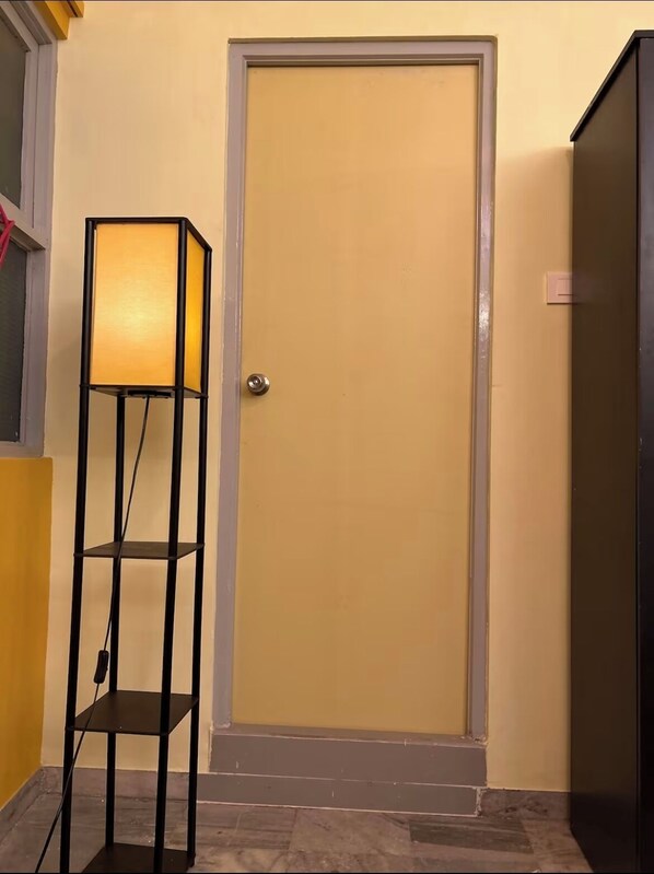 A room with a closed door, a floor lamp, and a partial view of a window.