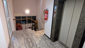 A hallway with a marble floor, a fire extinguisher mounted on the wall, and a staircase with a handrail.