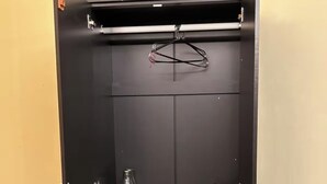 A black wardrobe with a hanging rack, a glass bottle, and a kettle on the shelves.