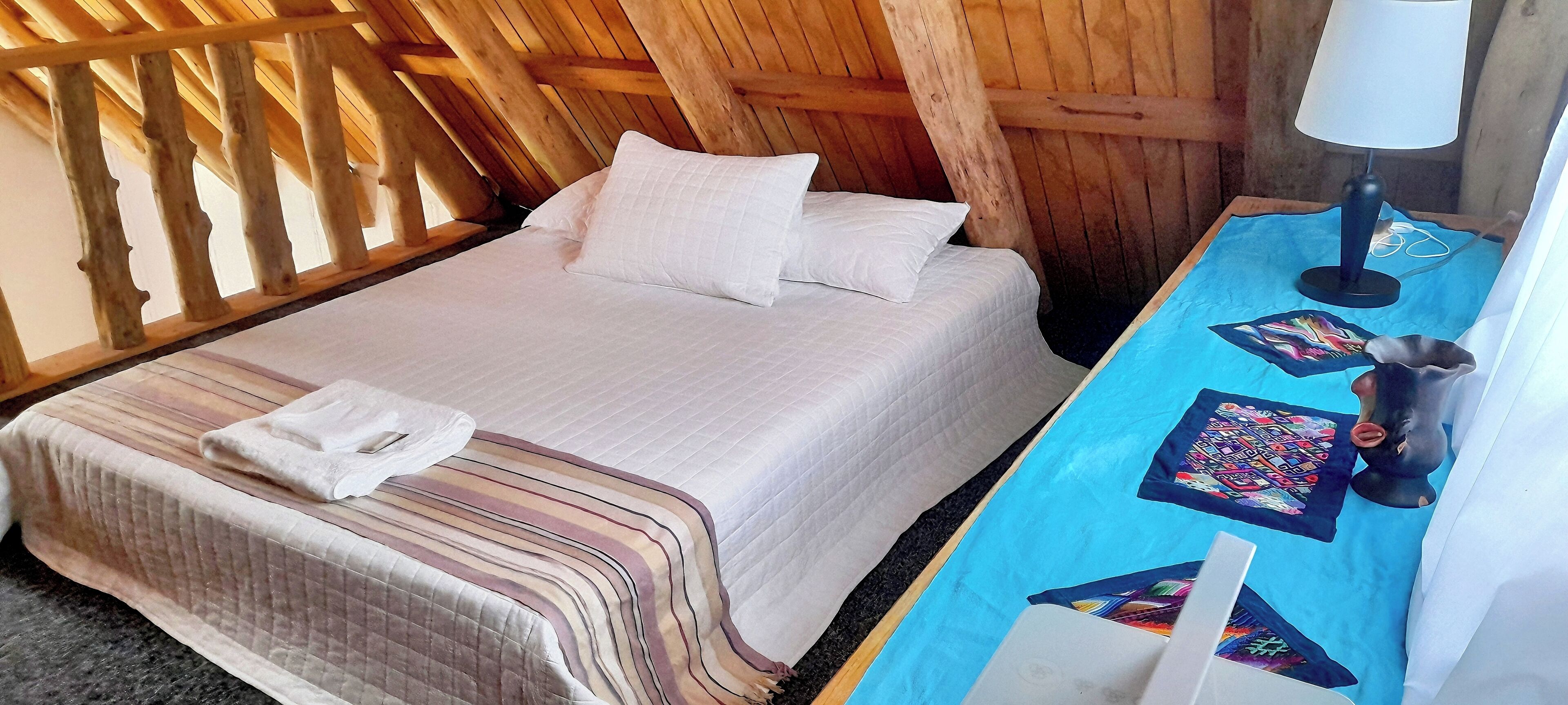 Een kamer met een bed, een nachtkastje met een lamp en een gewatteerd deken.