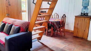 A cozy room with a sofa, wooden dining table, chairs, and a ladder. - El Colibri Cabin (San Juan La Laguna)