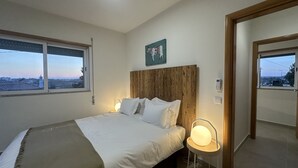 Een slaapkamer met een bed, bedlampen, een houten hoofdbord, een raam met uitzicht en een deur.