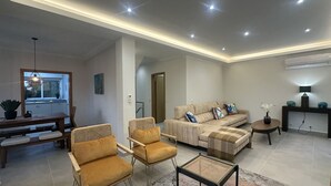 Een moderne woonkamer met een bank, twee fauteuils, een salontafel en een eethoek met een tafel en stoelen.