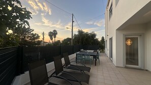 Une terrasse avec une table et des chaises, une clôture noire et un bâtiment doté d’une porte et d’une fenêtre.