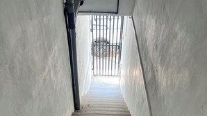 Eine schmale Treppe mit Holzboden, die nach oben führt, gesäumt von schlichten weißen Wänden, und mit einem Metallgitter am oberen Ende.