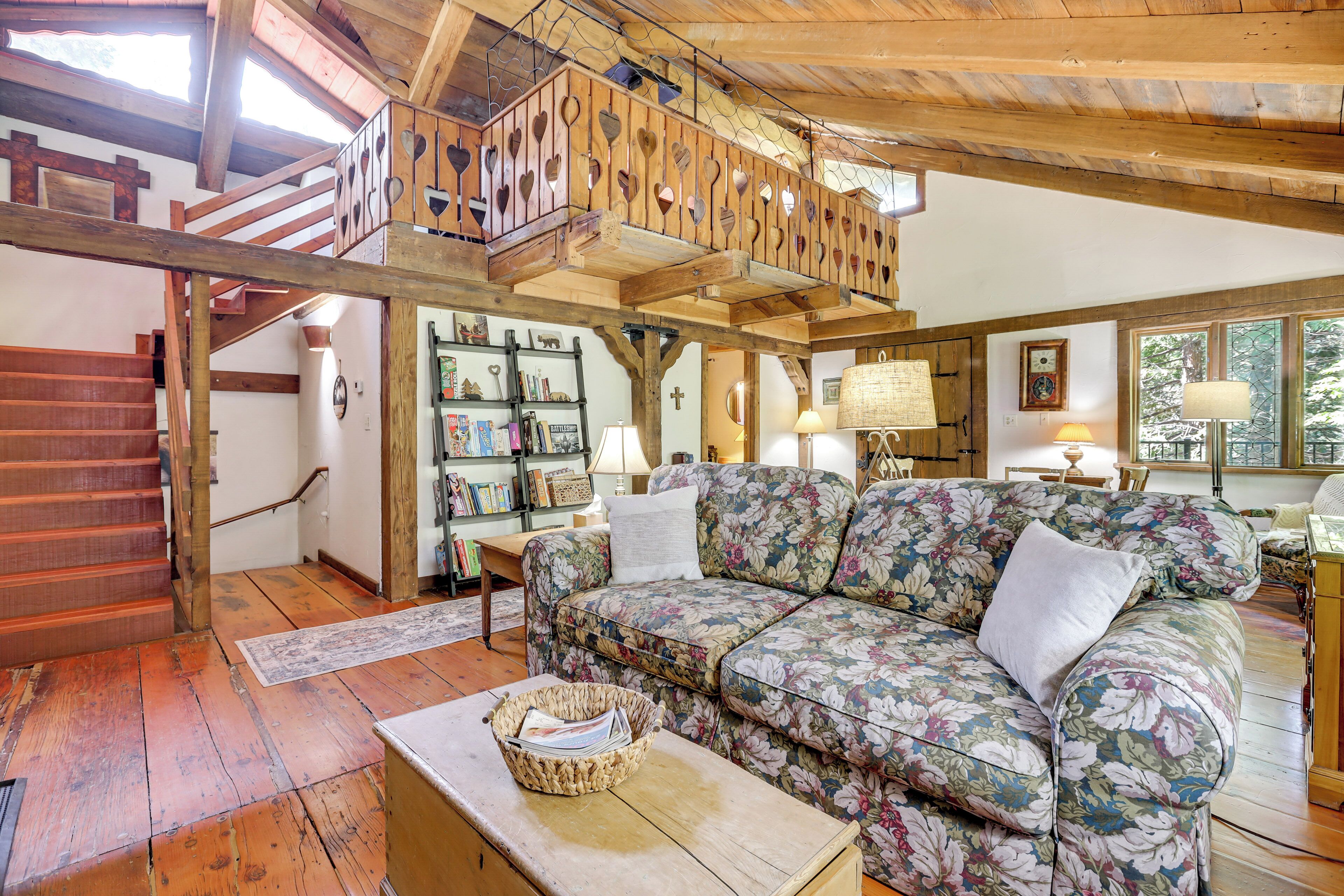 A spacious living area with a wooden staircase, a floral sofa, and a bookshelf.