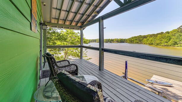 Une terrasse couverte avec vue sur une rivière, une chaise, une table et un kayak.