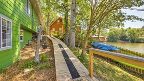 Une terrasse en bois menant à un lac, entourée de verdure et d’une serre.