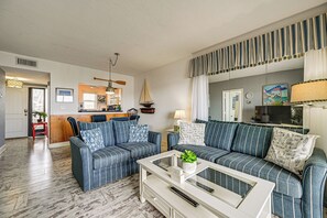 A living room with striped sofas, a coffee table, and a kitchen area in the background.