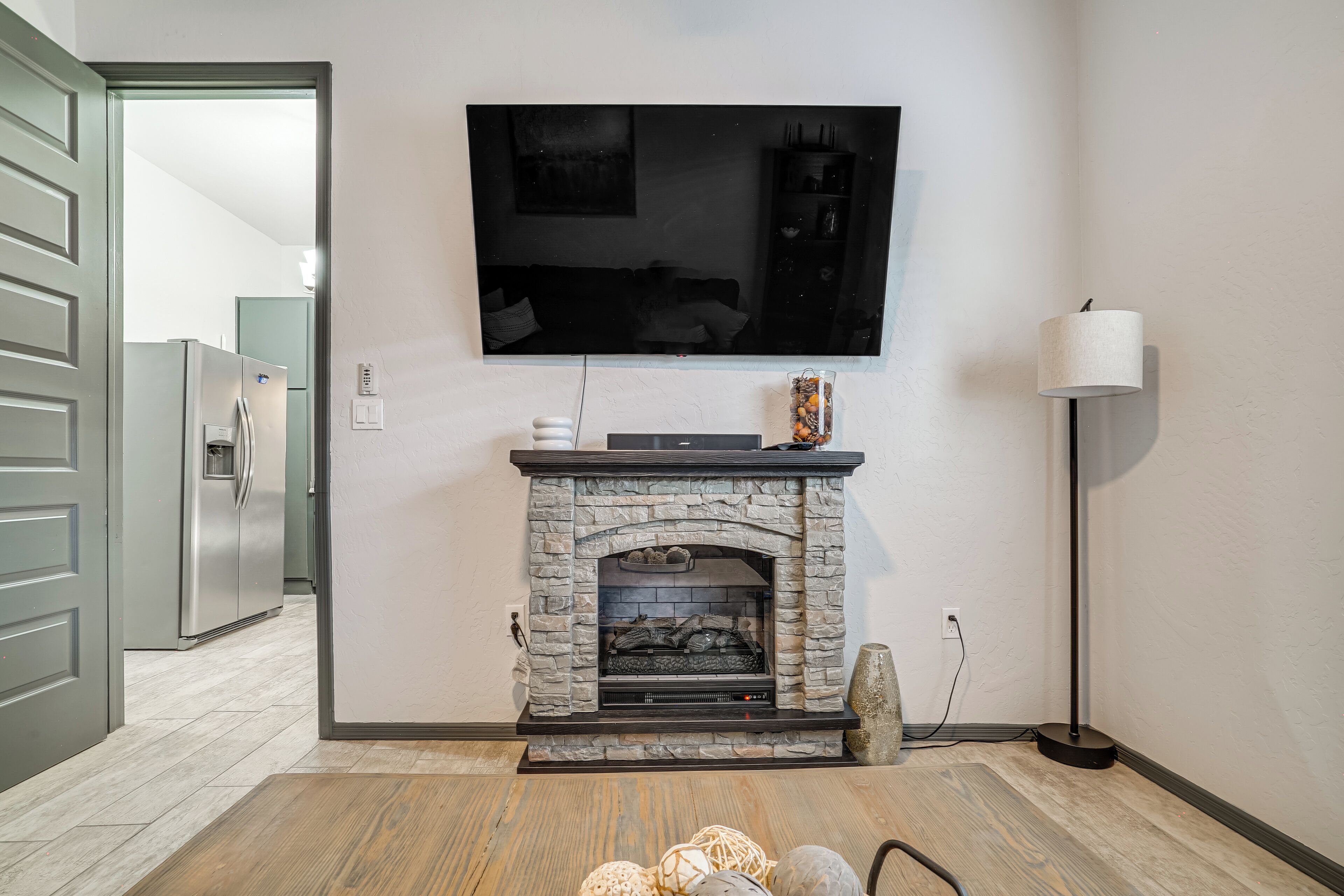 Ein modernes Wohnzimmer mit Kamin aus Stein, einem flachbildfernseher darüber, einem Kühlschrank und einer Stehlampe.