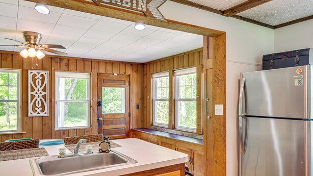 Eine Küchenzeile in einer Holzhütte, mit Wandverkleidung aus Holz, einem Edelstahlkühlschrank, einer Spüle und einem Deckenventilator.