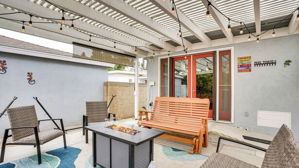 Eine Terrasse im Freien mit einem Feuerkorb-Tisch, Korbstühlen, einer Holzbank und Lichterketten.