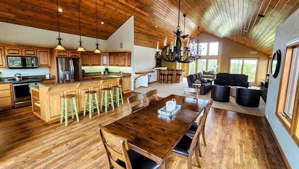 Una cocina amplia con armarios de madera, una isla central con taburetes, una mesa de comedor con sillas, y una zona de estar con sofá y sillones.