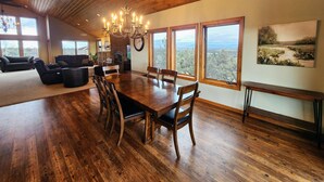 Un comedor espacioso con una mesa y sillas de madera, ventanas amplias que ofrecen vistas al exterior y una araña colgando del techo.