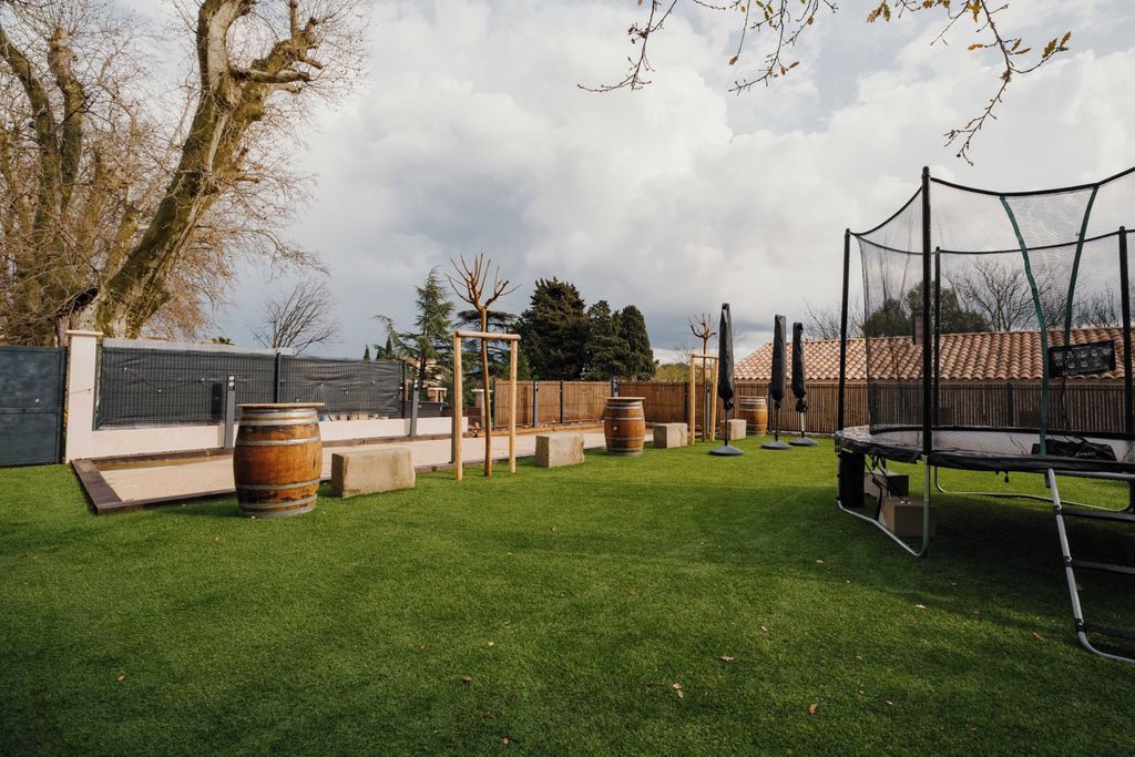 Ein Garten mit Kunstgrasanlage, einem Trampolin und Holzböllen.