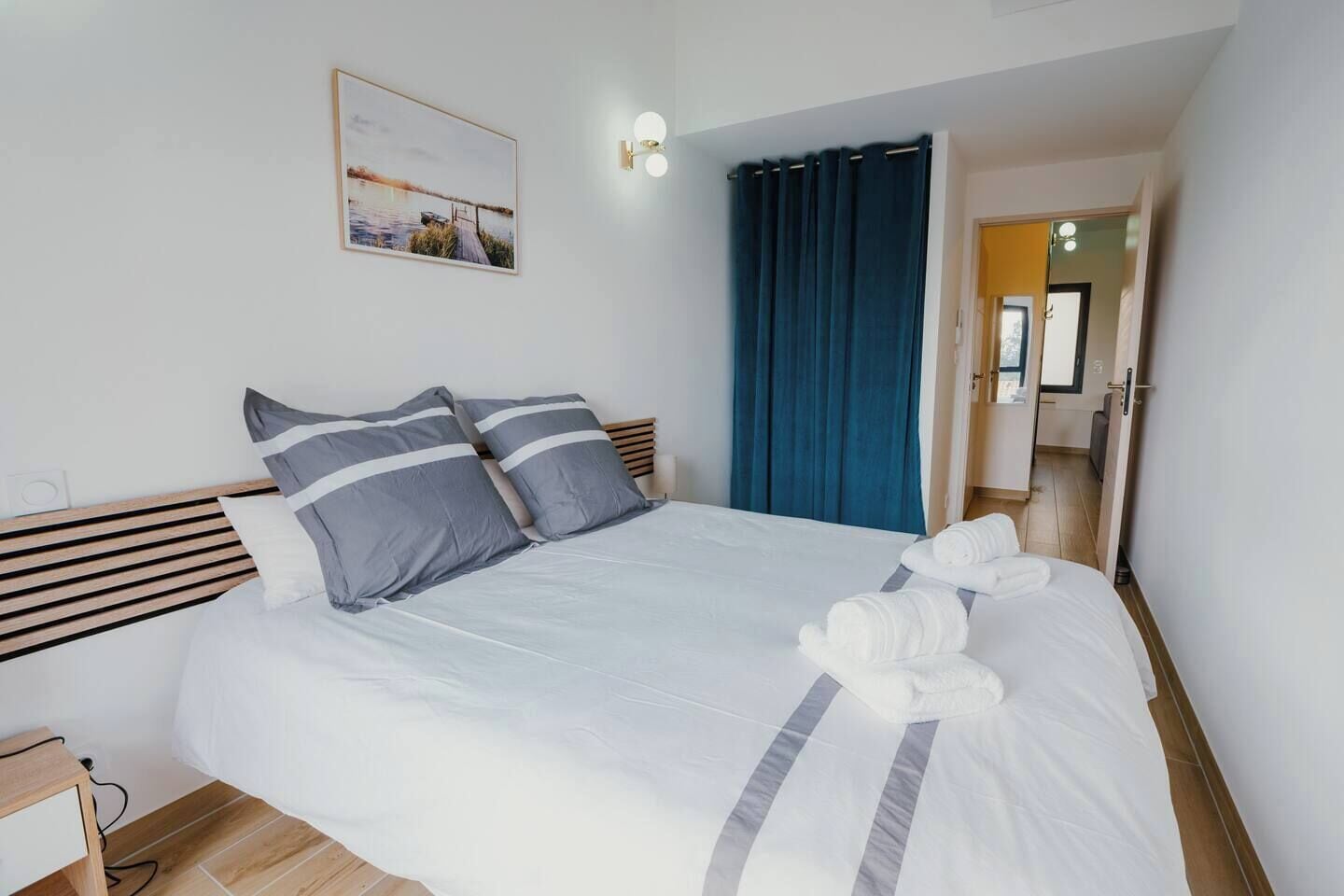 A neatly made bed with white and gray bedding, a wooden headboard, and a wall-mounted picture.