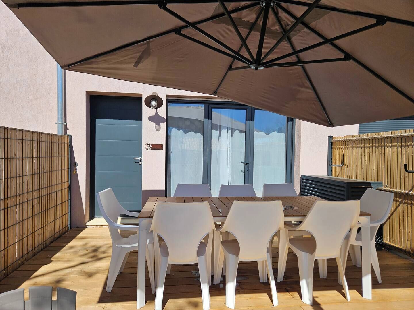 Une terrasse extérieure avec une table et des chaises, un grand parasol et une porte-fenêtre coulissante.