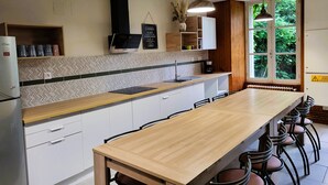 A modern kitchen with a long wooden table, white cabinets, and a built-in oven. - Gîte du Château - 18 people - Centre de la France - au coeur du Berry (Cluis)