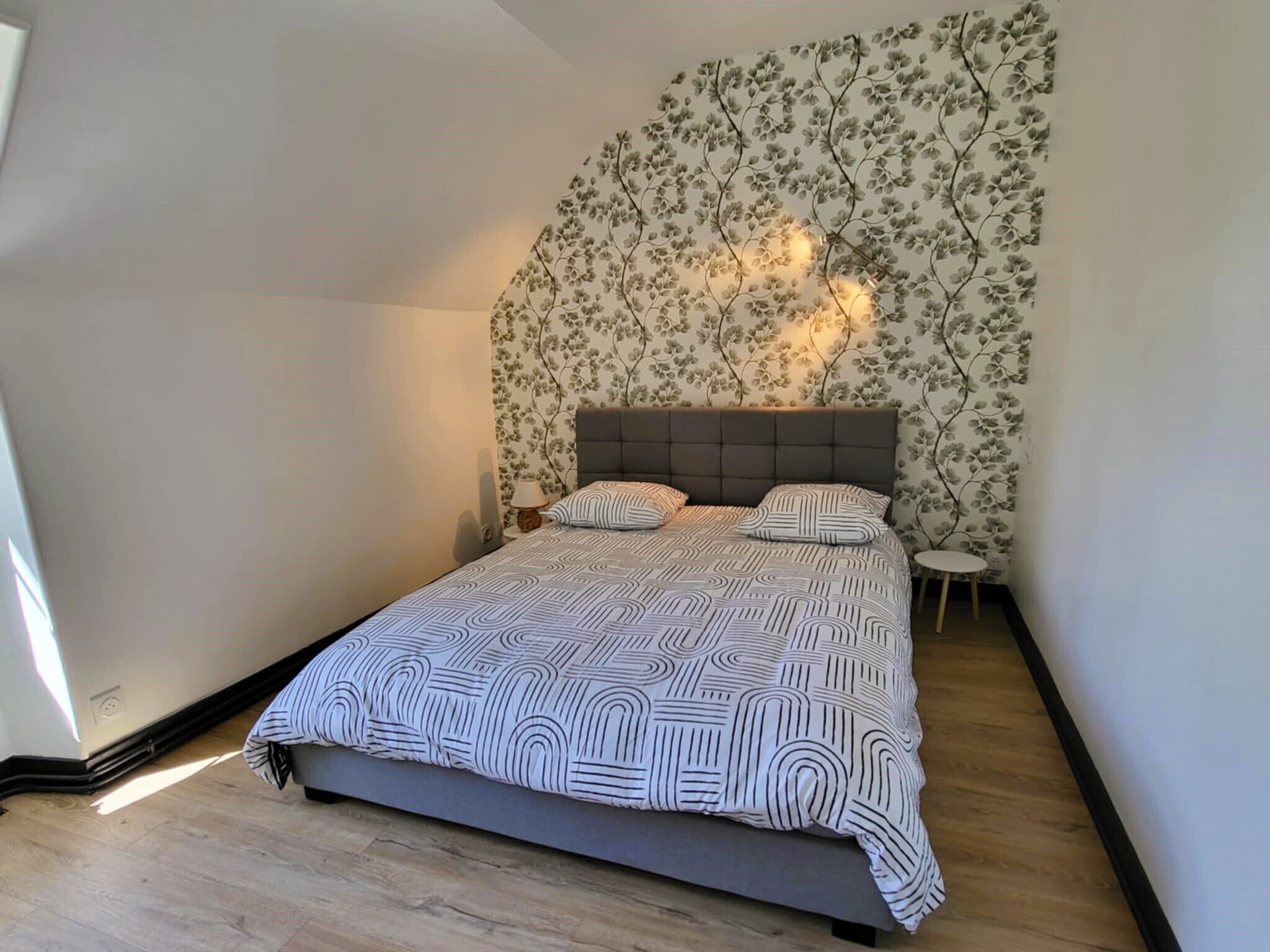 Ein Schlafzimmer mit einem Bett, einem Nachttisch, einer Lampe und einer Wand mit Blumenmuster-Tapete.