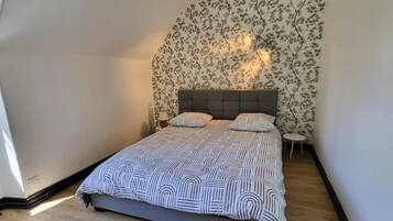 Ein Schlafzimmer mit einem Bett, einem Nachttisch, einer Lampe und einer Wand mit Blumenmuster-Tapete.