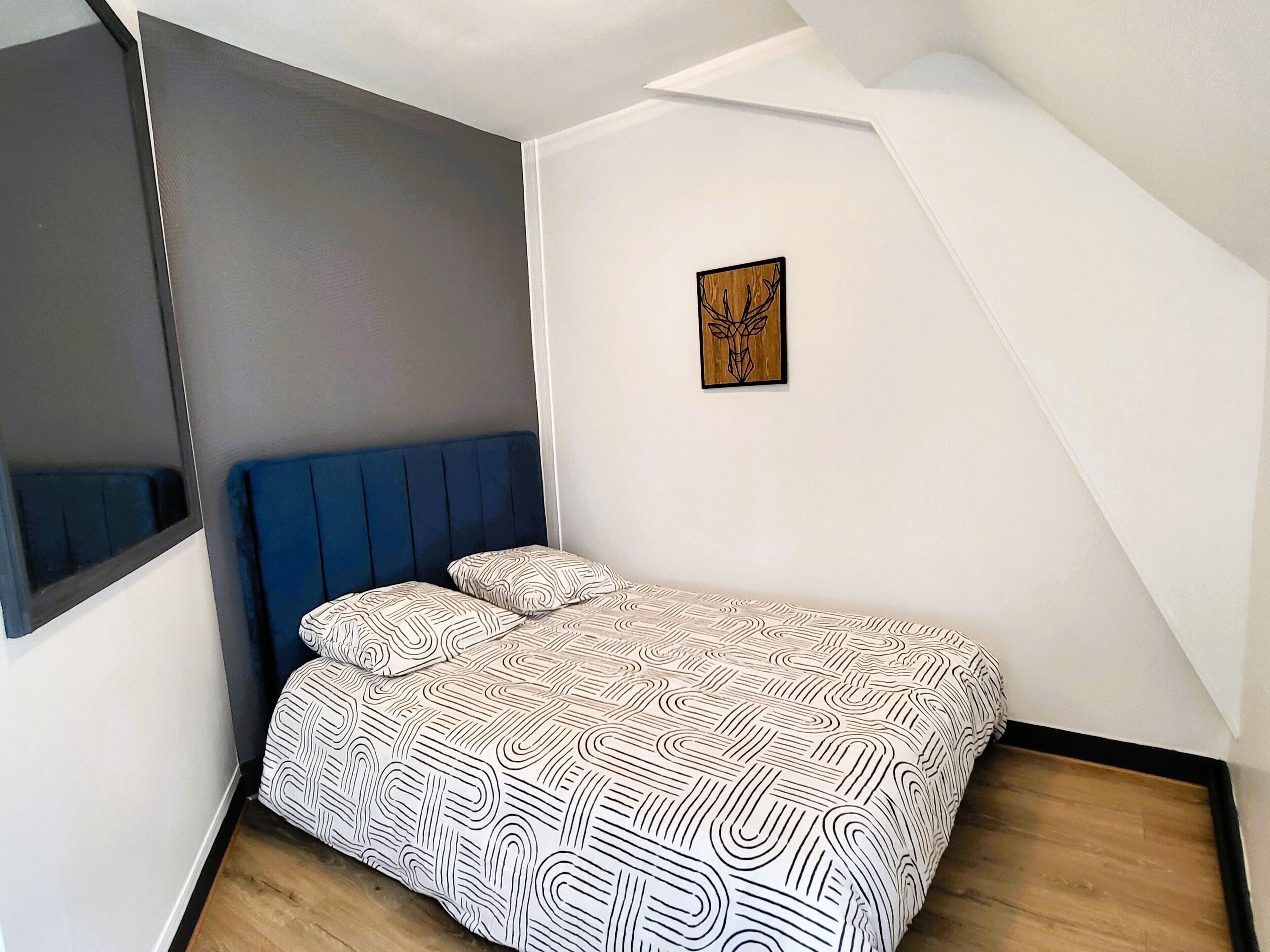 A bedroom with a bed, a blue headboard, a wall-mounted picture, and a sloped ceiling.