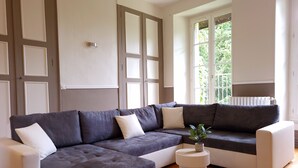 A modern living room with a sectional sofa, a round side table, and a view of greenery outside. - Gîte du Château - 18 people - Centre de la France - au coeur du Berry (Cluis)