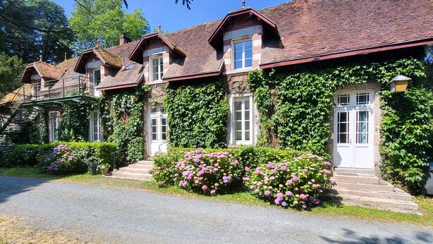 A row of traditional houses with brick walls and red-tiled roofs, surrounded by lush greenery and flowering plants. - Gîte du Château - 18 people - Centre de la France - au coeur du Berry (Cluis)