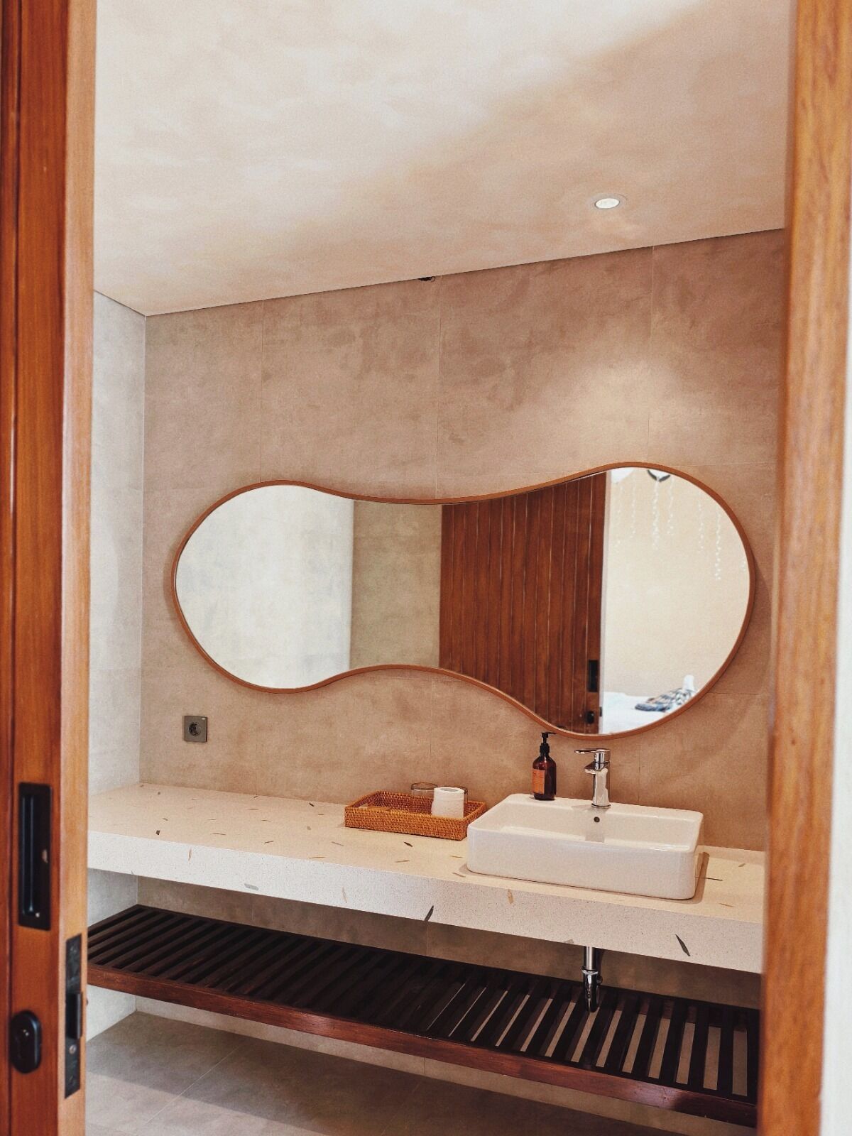 Un baño con un espejo ovalado grande, un lavabo blanco y un estante de madera.