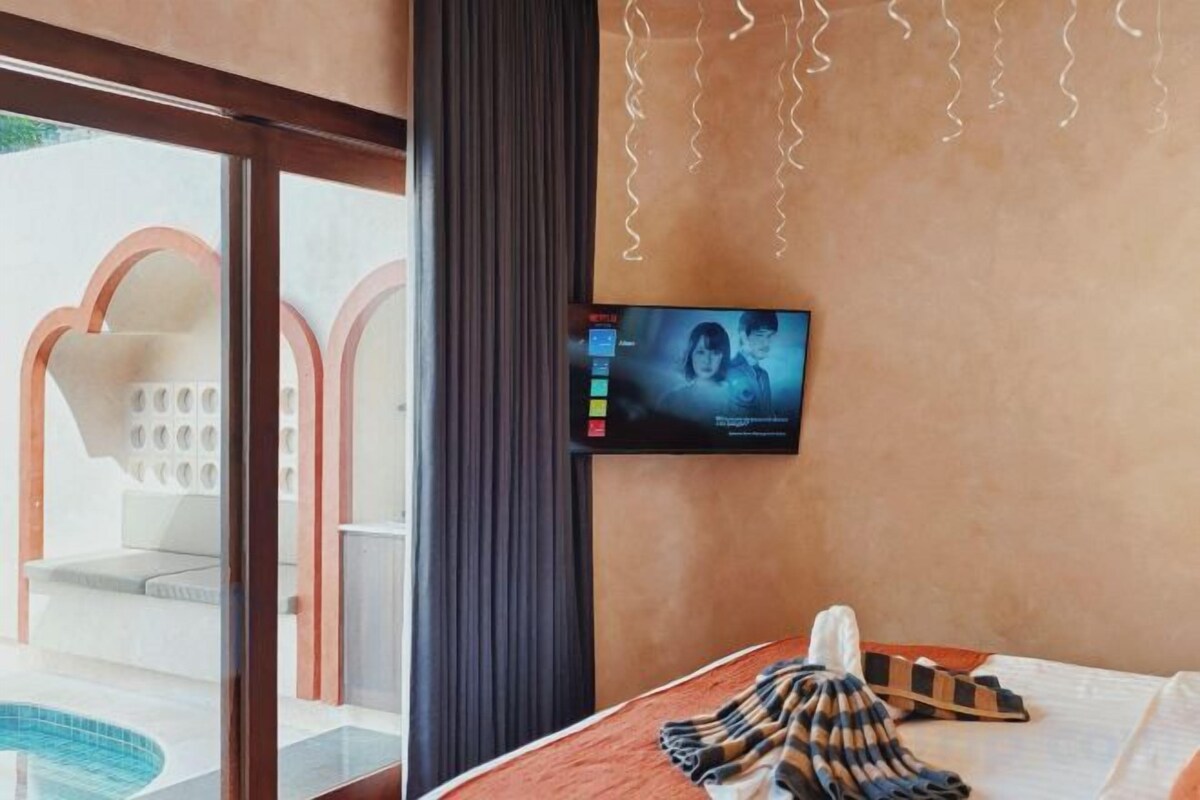 A hotel room with a television mounted on the wall, a bed with a striped blanket, and a view of the outdoor seating area.