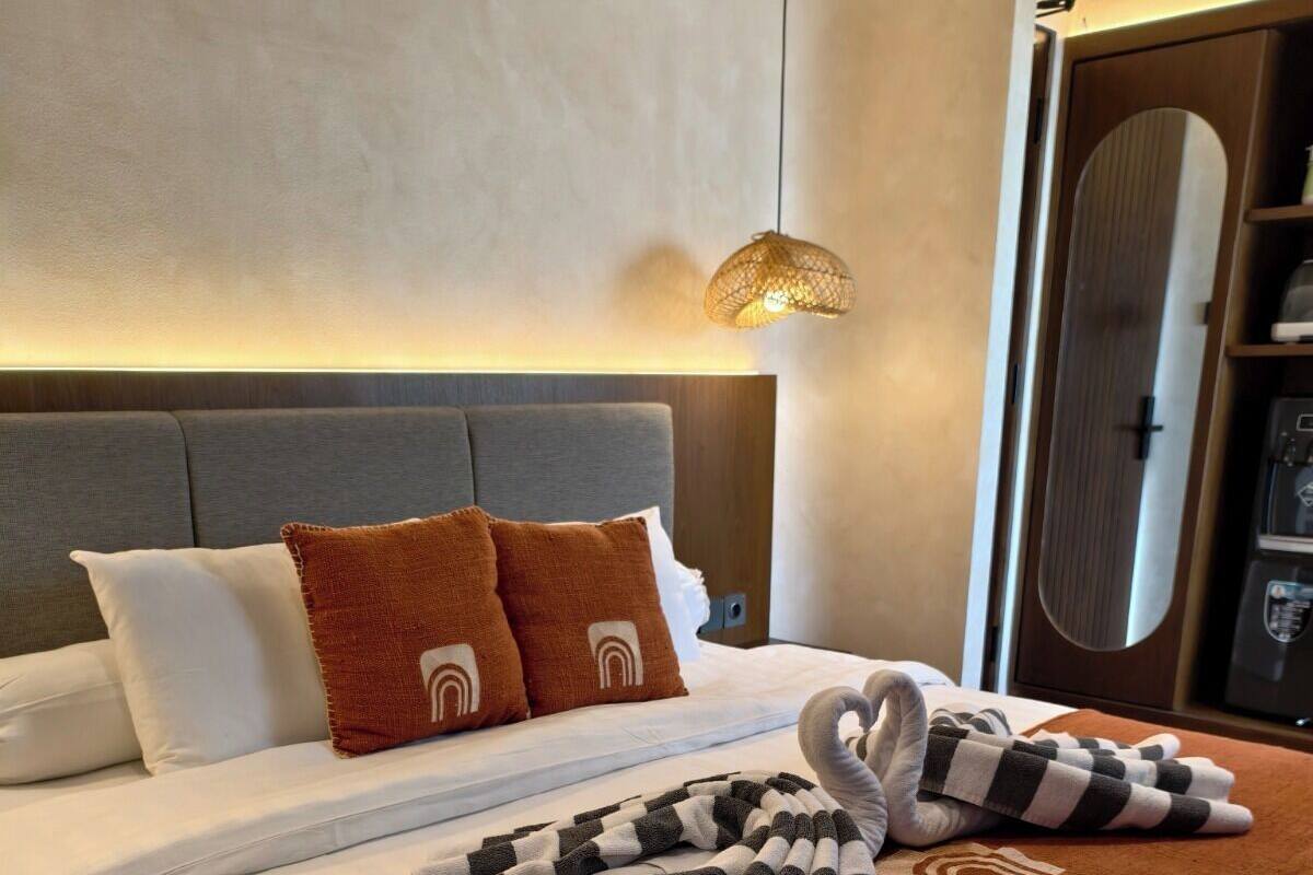 Ein ordentlich bezogenes Bett mit einer braunen Tagesdecke, einem gestreiften Handtuch und zwei Kissen mit einem besonderen Design.