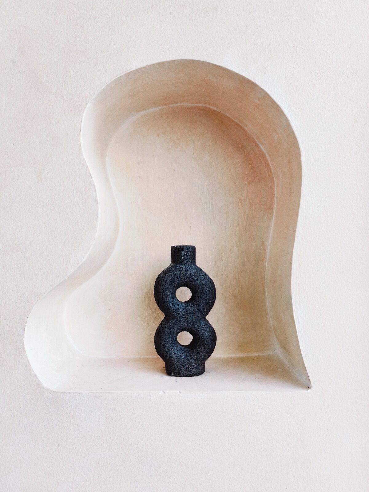 Una escultura de pared abstracta y original, con una base de color claro y un objeto circular negro en la parte superior.