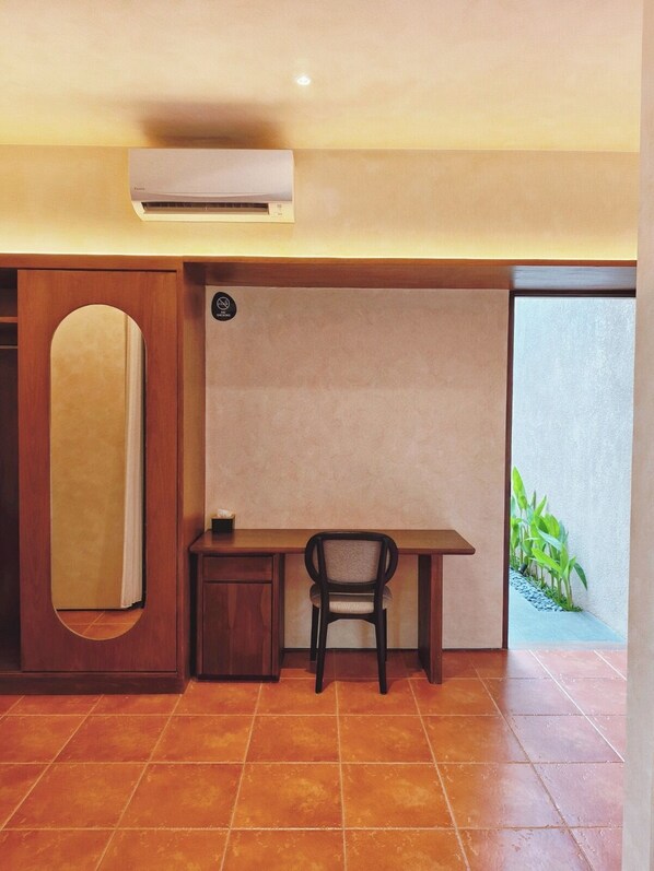 Habitación compacta con escritorio, silla y un mueble pequeño. Un equipo de aire acondicionado está instalado en la pared sobre el escritorio.