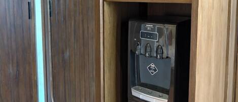 A compact kitchen with a built-in water dispenser, a microwave, and a shelf with dishes.