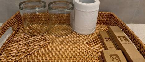 A wicker basket containing three glass jars, a roll of toilet paper, and two cardboard boxes with branding.