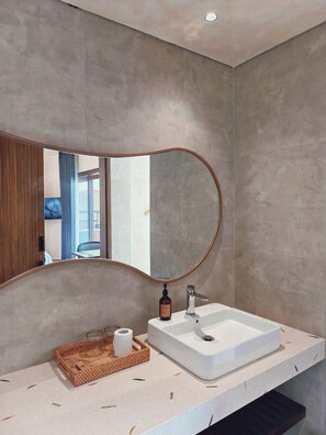 Un baño moderno con un espejo grande, un lavabo blanco y una cesta de madera con artículos de aseo.