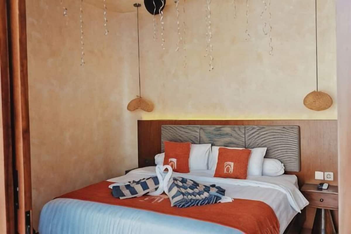 Ein Schlafzimmer mit Bett, Kissen, Nachttisch und einer Pendelleuchte.