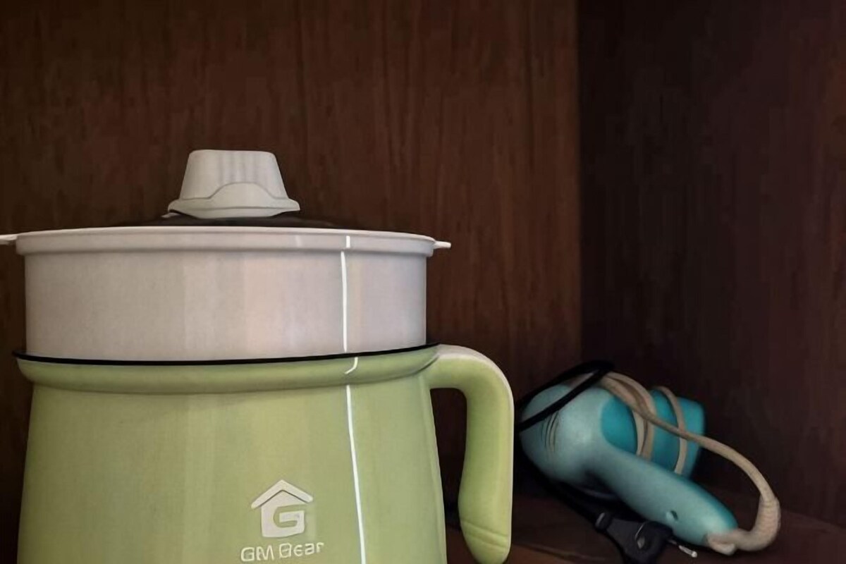 A green GABA Bear slow cooker with a lid and handle, placed on a wooden surface next to a teal bag.