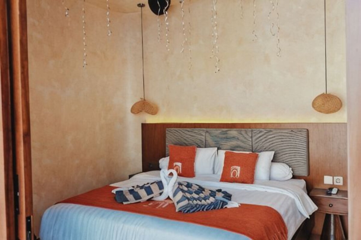 A bedroom with a bed, pillows, a bedside table, and a hanging light fixture.