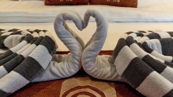 A bed with two pillows, a heart-shaped towel arrangement, and a towel with "Allure Villa" embroidered on it.
