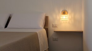 A neatly made bed with white linens and a beige blanket, a wall-mounted light fixture, and a wooden shelf with a switch. - Tenuta Petra Chiara -Apulian Country B&B (Nardo)