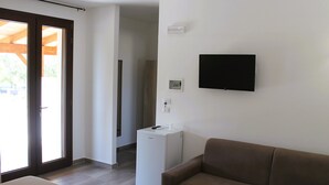 A room with a brown sofa, a white refrigerator, a flat-screen TV mounted on the wall, and a sliding glass door leading to an outdoor area. - Tenuta Petra Chiara -Apulian Country B&B (Nardo)