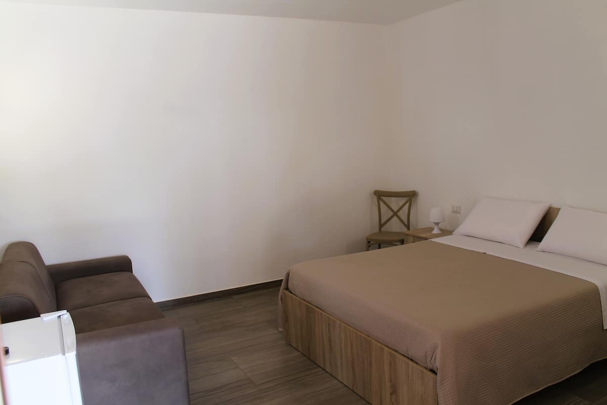 A bedroom with a bed, a sofa, a small table, and a lamp.