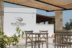Ein Außenbereich mit Korbmöbeln und einer weißen Wand, auf der das Logo und der Name Tenuta Petra Chiara abgebildet sind.