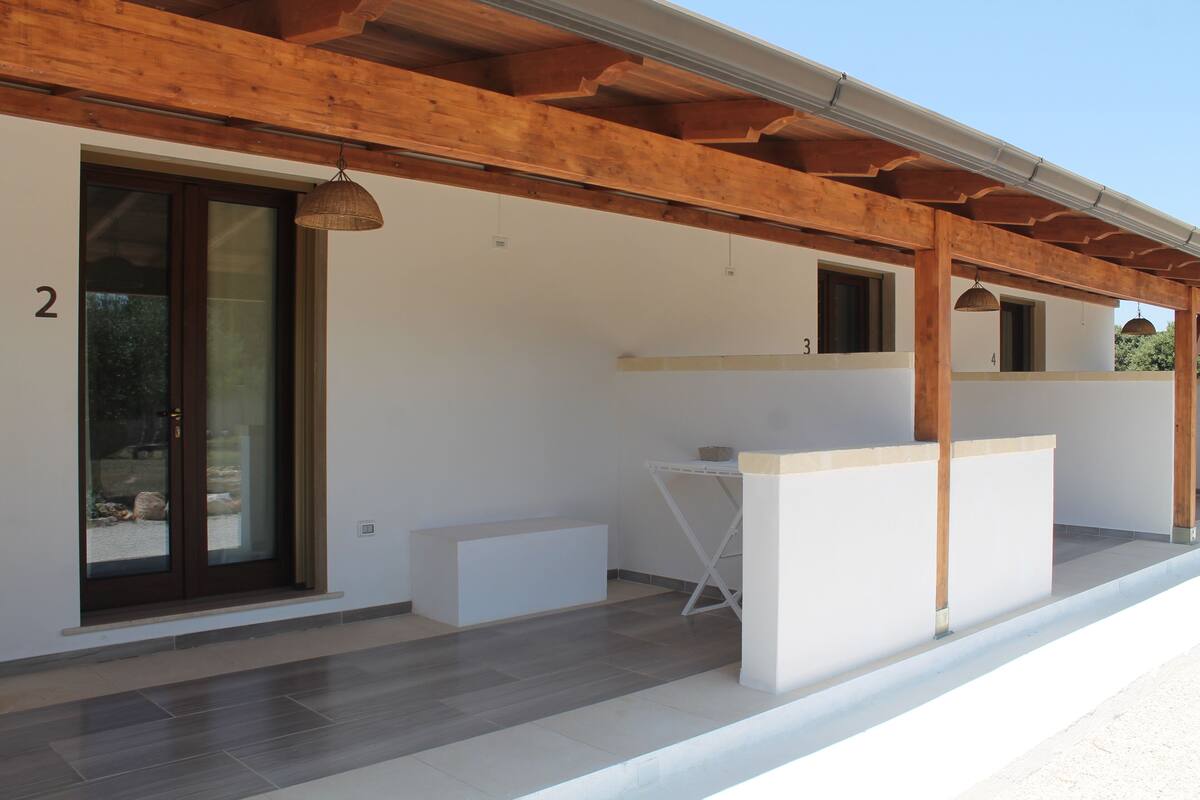 A modern building with a wooden facade, numbered rooms, and a covered outdoor area with a table and chairs.