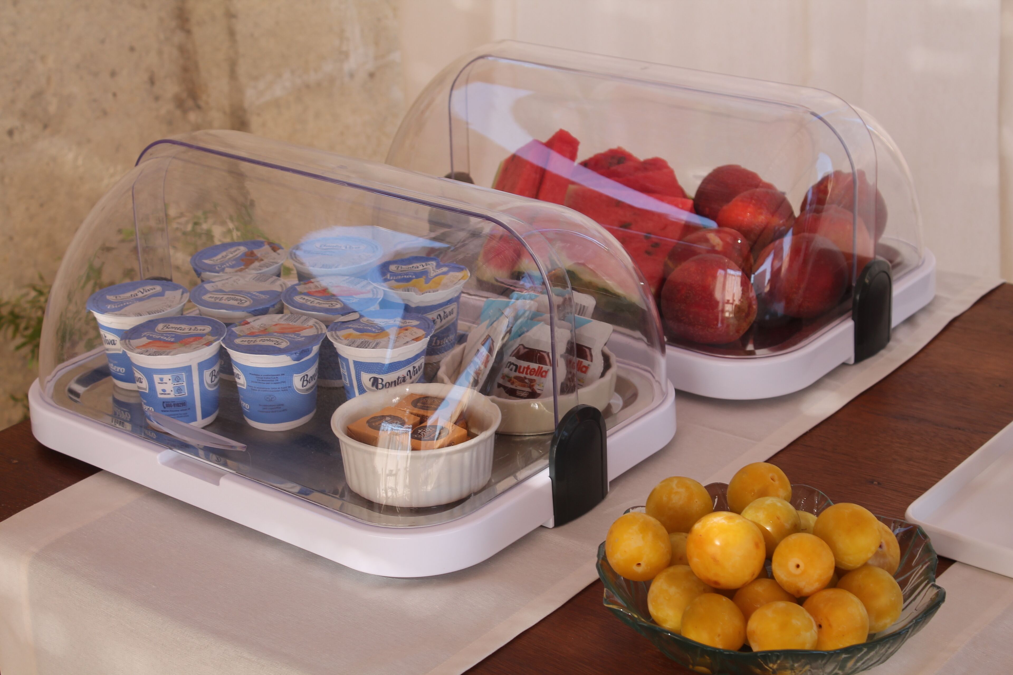 A buffet with covered food items including yogurt, Nutella, and fruits.
