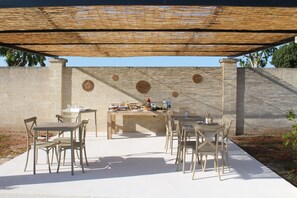 An outdoor patio with a table and chairs, a woven shade structure, and a stone wall with circular designs. - Tenuta Petra Chiara -Apulian Country B&B (Nardo)